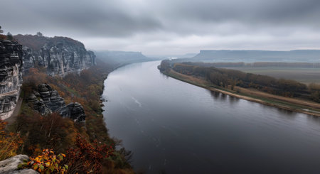 The tranquil river winds through steep cliffs adorned with autumn foliage, creating a serene atmosphere. Fog hangs gently in the early morning light, enhancing the beauty of the natural landscape.の素材