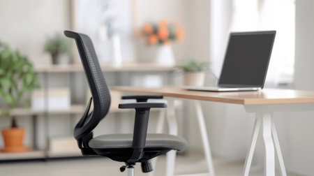 A sleek black office chair is positioned beside a wooden desk with a laptop. The workspace is bright, featuring potted plants and decorative elements in the background, creating a welcoming and productive atmosphere.の素材