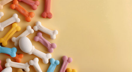 A variety of colorful dog treats shaped like bones and an oval, scattered across a soft yellow surface, perfect for rewarding pets and enhancing their mealtime experience.の素材