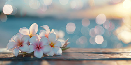 A cluster of frangipani flowers rests on a wooden table by the seaside, illuminated by the warm hues of sunset. Soft bokeh from the water enhances the tranquil atmosphere.の素材