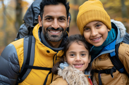 A father and his three children enjoy a joyful moment while hiking in a vibrant autumn forest, surrounded by colorful leaves and nature. They wear warm jackets and backpacks as they smile at the camera.の素材