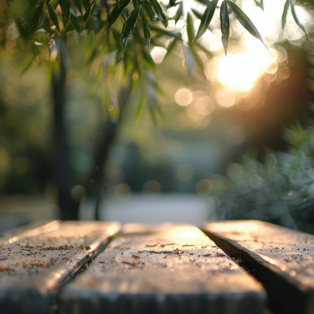 Soft sunlight pours through leafy branches, illuminating a rustic wooden table in a tranquil outdoor setting during the evening hours. The atmosphere feels calm and inviting, surrounded by greenery.の素材