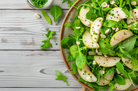 A vibrant salad combines fresh arugula, sliced pear, and chopped nuts, garnished with herbs. The dish is served on a rustic wooden table, creating an inviting and healthy dining experience.の素材