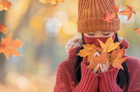 A woman dressed in a cozy red sweater gathers vibrant autumn leaves in her hands, surrounded by a blurred forest backdrop filled with the warm hues of fall.の素材