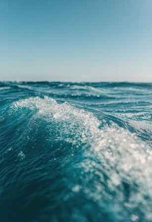Turquoise waves gently crash and ripple across the water's surface, reflecting sunlight and creating a sparkling effect. A backdrop of fluffy clouds fills the sky on a calm day by the ocean.の素材