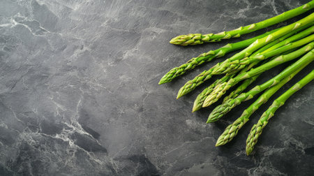 A bunch of vibrant green asparagus spears lay next to fresh parsley on a dark textured surface, highlighting the freshness and color of the vegetables.の素材