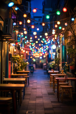 A wooden table sits in the foreground of a lively outdoor space filled with string lights. The soft glow creates a warm atmosphere, inviting patrons to enjoy their meals in the bustling urban environment as evening settles in.の素材