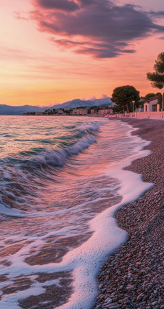 Gentle waves roll onto a warm sandy beach at sunset, reflecting shades of orange and pink in the sky. Footprints lead towards the serene shoreline under a colorful cloudscape.の素材