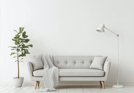 A gray sofa with a cozy blanket draped over it sits in a minimalist living room. A sleek floor lamp illuminates the space, accompanied by a potted plant, creating a warm atmosphere.の素材