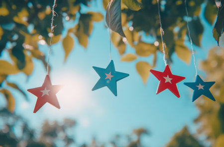 Bright red and blue stars are strung on a line, catching the sunlight as they dangle amongst green leaves, creating a festive and cheerful atmosphere on a sunny day.の素材