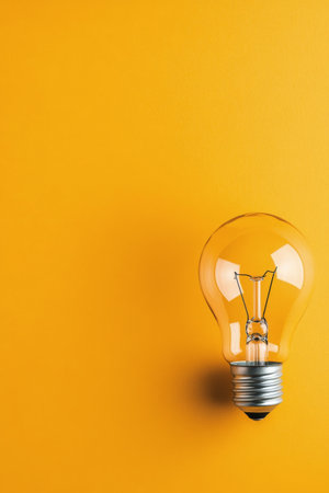 The light bulb rests upright against a vibrant yellow backdrop, highlighting its glass design and metal base. It symbolizes brightness and innovation in a minimalist style.の素材