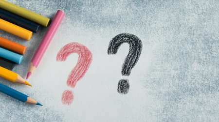 Three colored pencils are resting next to a chalk question mark drawn on a dark surface. The composition captures a moment of curiosity and creativity in a daylight setting.の素材