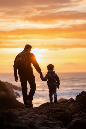 A father and his young son stroll along a rugged coastline, holding hands as the vibrant sunset paints the sky. They embrace the beauty of nature and share a cherished moment.の素材