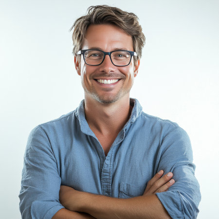 A smiling man stands with arms crossed, wearing glasses and a dark shirt. He exudes confidence and warmth, set against a light background, creating a friendly and inviting atmosphere.の素材