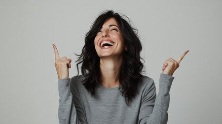 A woman is filled with excitement as she laughs wholeheartedly, her joyful expression reflecting happiness. She raises her hands enthusiastically while dressed in a soft sweater.の素材