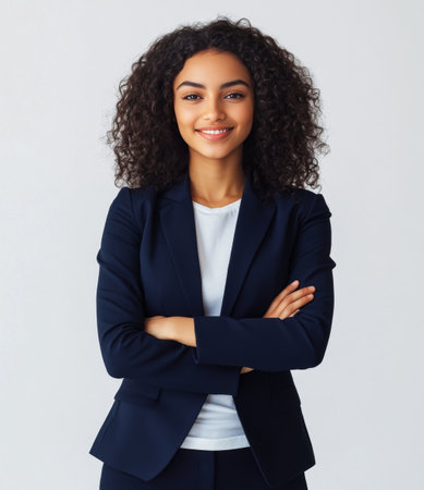 A young woman with curly hair confidently stands with her arms crossed, wearing a navy blazer and a white shirt, showing professionalism and poise.の素材