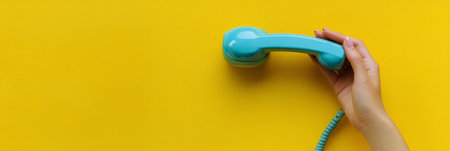 A hand grips a retro blue telephone receiver, contrasted against a cheerful yellow backdrop, evoking a sense of nostalgia and communication in a lively environment.の素材