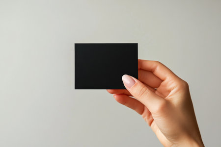 A hand displays a small, blank black card against a light colored background, showing its simplicity and versatility. The bright lighting emphasizes the smooth surface.の素材