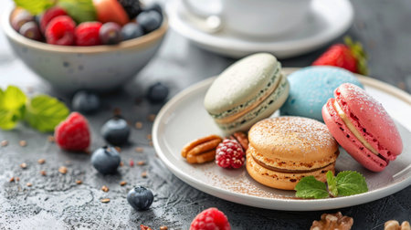 Four macarons with various colors on a white plate with fresh berries and pecans, on a gray textured surface.の素材