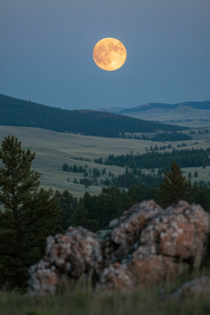 A vibrant full moon illuminates the twilight sky, casting a warm glow over the rolling hills and lush trees of a tranquil landscape at dusk.の素材