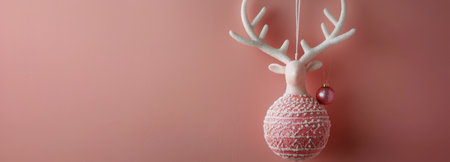 A white reindeer ornament with pink details hangs on a pink wall, with a single pink ornament dangling from its antlers.の素材