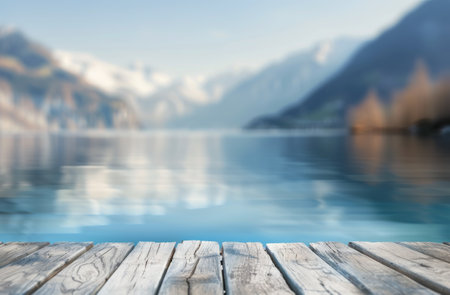 A wooden dock extends out over a still lake, with a blurred background of mountains and trees. The surface of the water is calm and reflective.の素材