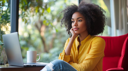 A young woman sits thoughtfully in a modern chair at her desk, focused on her laptop while natural light floods the spacious workspace filled with plants and stylish decor.の素材