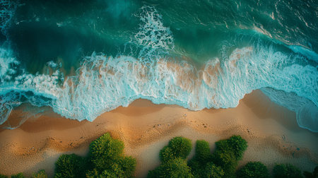 An aerial view of turquoise ocean waves crashing on a sandy beach, with green vegetation lining the shore.の素材