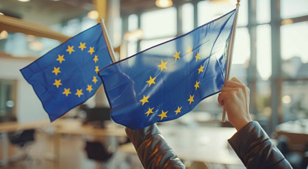 A person holds two European Union flags in an office building.の素材
