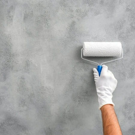 A hand wearing a white glove holds a paint roller that is applying gray paint to a textured wall. This shows the process of home improvement and interior decoration.の素材