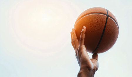 In a lively outdoor setting, two hands stretch upward to catch a basketball soaring through the sky. The sun casts a bright light, enhancing the energetic atmosphere of the game.の素材