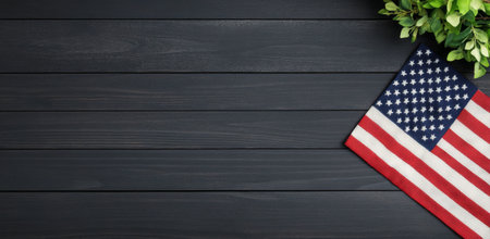 An American flag is positioned on a dark wooden surface, partially covered by lush green foliage. The colors of the flag stand out against the background, creating a patriotic display.の素材