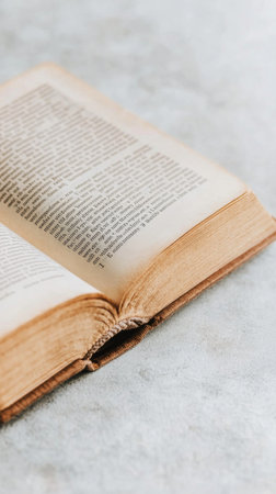An open book is placed on a rustic wooden surface. The pages are slightly yellowed, showing signs of age, while soft lighting enhances the natural textures of the wood and paper.の素材