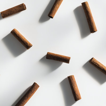 Cinnamon sticks are shown suspended in mid air, surrounded by a cloud of finely ground cinnamon. The arrangement highlights their rich brown color and textured surface.の素材