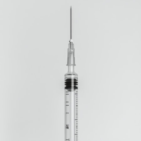 A clear medical syringe stands upright against a plain background, showing its design and structure. The needle is sharp and precise, ready for medical use.の素材