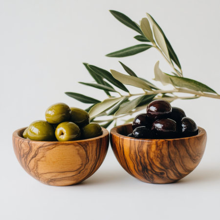 Two wooden bowls display green and black olives alongside fresh olive leaves, showing the natural beauty of these culinary delights in a rustic atmosphere.の素材