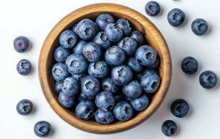 A wooden bowl filled with vibrant blueberries showcases their deep blue color, surrounded by a few scattered berries. Perfect for healthy desserts or snacks.の素材