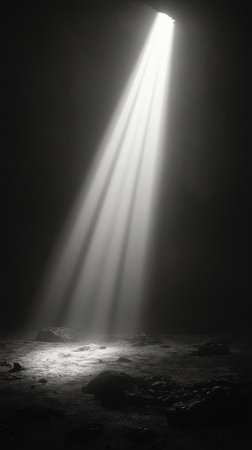Brilliant shafts of light filter through an opening above, illuminating suspended particles in a deep, dark underwater setting. The contrast creates a mesmerizing effect.の素材