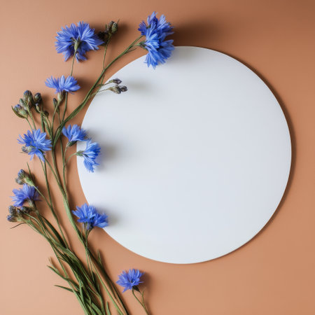 Fresh blue flowers are artistically placed next to a blank white circle on a soft orange surface, creating a calm and inviting composition perfect for design projects.の素材