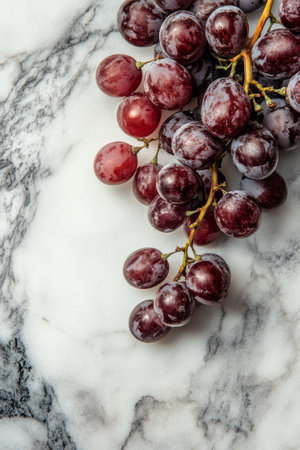 Clusters of red grapes rest on a sleek marble background, highlighting their natural shine and inviting texture. The contrast enhances the fruit's rich hue and freshness.の素材