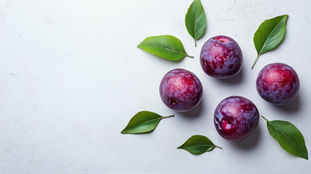 Plums with purple deep hues are arranged around fresh green leaves on a light surface, showing their vibrant colors. This display highlights the natural beauty of the fruits.の素材