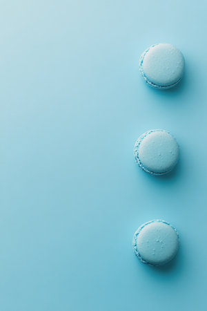Three blue macarons sit elegantly on a smooth pastel blue surface, showing their vibrant color and delicate texture. This dessert offers a delightful treat for any occasion.の素材