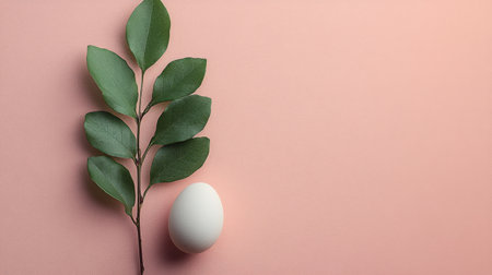 A white egg rests beside a branch of fresh green leaves on a soft pink background, showing a simple yet elegant composition ideal for minimalist decor.の素材
