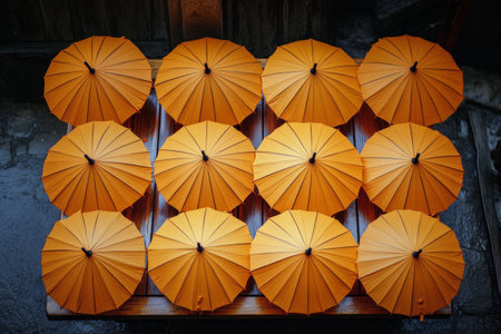 Bright orange paper umbrellas are arranged in a symmetrical pattern on a wooden table. Lush greenery in the background adds a tranquil atmosphere, suggesting a peaceful outdoor setting.の素材
