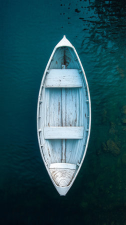 A weathered white rowing boat floats serenely in a foggy lake, surrounded by trees. The still water creates a perfect reflection of the boat, enhancing the tranquil atmosphere.の素材