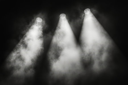 Bright stage lights beam down through swirling smoke, creating a dramatic atmosphere in a theater. The ambient scene suggests an upcoming performance or event.の素材