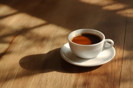 A cup of coffee with intricate latte art sits on a wooden tray beside cookies and coffee beans, illuminated by warm natural light in a calm setting.の素材