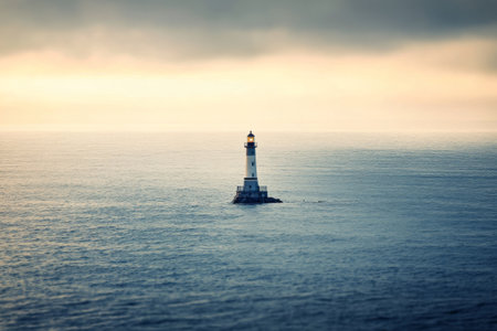 A weathered lighthouse rises from the calm ocean waters as the sun begins to rise, casting a soft glow on the structure while reflecting on the waves.の素材