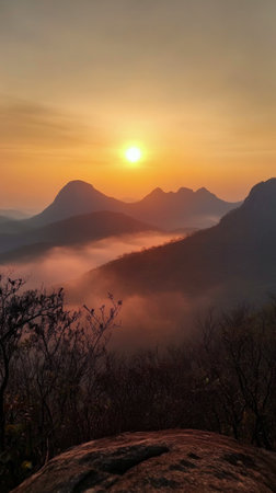 A stunning sunset illuminates the rugged mountain peaks as mist swirls in the valley below. The warm colors create a serene and captivating atmosphere in the landscape.の素材