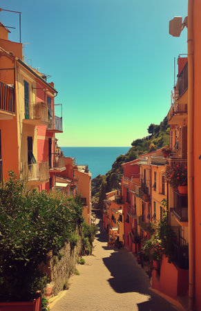 A vibrant street lined with pastel-colored buildings leads down towards the sparkling ocean. Lush greenery frames the path, creating a picturesque coastal scene.の素材